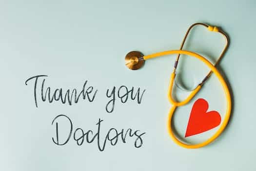 From above arrangement of yellow stethoscope with red heart shape placed on blue background with THANK YOU DOCTORS inscription