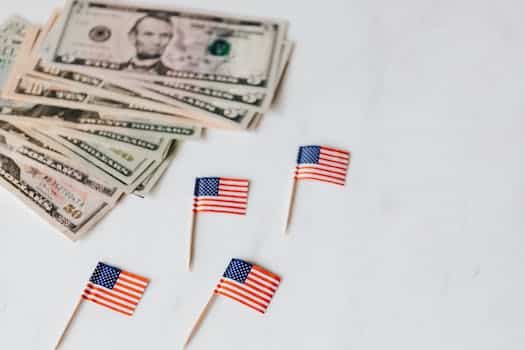 From above of flags of United States of America on toothpicks placed near bundle of American dollars of different nominal pars on white surface of table