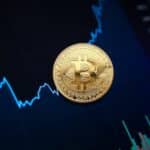 Golden bitcoin coin on background of chart showing indicators of changes in cryptocurrency rates