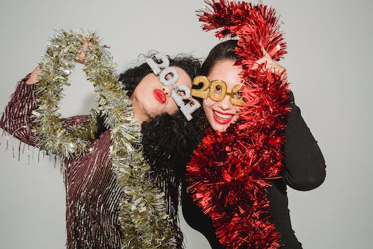 Happy women wearing festive dresses and 2021 glasses wrapped with shiny tinsel while celebrating New Year